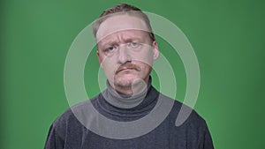 Portrait of blonde middle-aged man in gray pullover sadly turning his head to refuse or disagree on green background.