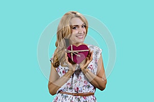 Portrait of blonde middleaged woman holding a heart shape gift box in both hands.