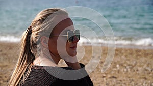 Portrait blonde sea beach. A woman is sitting by the sea, wearing a black sweater and sunglasses, enjoying the sea view