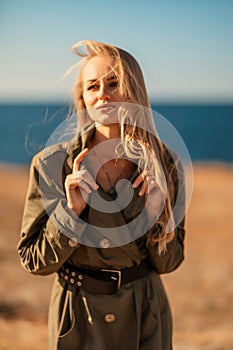 Portrait blonde sea cape. Calm young blonde in a khaki raincoat stands on the seashore