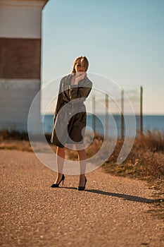 Portrait blonde sea cape. A calm young blonde in a khaki raincoat stands on the seashore against the backdrop of a