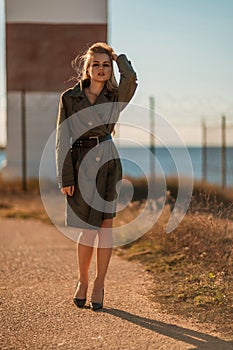 Portrait blonde sea cape. A calm young blonde in a khaki raincoat stands on the seashore against the backdrop of a