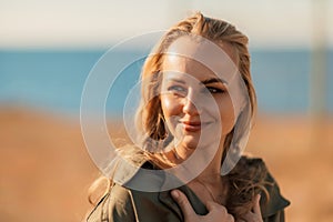 Portrait blonde sea cape. A calm young blonde in an unbuttoned khaki raincoat stands on the seashore, under the raincoat