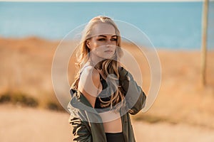 Portrait blonde sea cape. A calm young blonde in an unbuttoned khaki raincoat stands on the seashore, under the raincoat