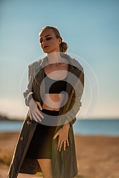 Portrait blonde sea cape. A calm young blonde in an unbuttoned khaki raincoat stands on the seashore, under the raincoat