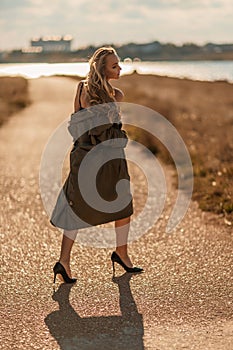 Portrait blonde sea cape. A calm young blonde in an unbuttoned khaki raincoat walks along the seashore, under a raincoat