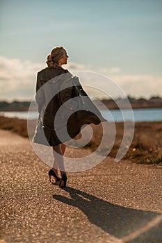Portrait blonde sea cape. A calm young blonde in an unbuttoned khaki raincoat walks along the seashore, under a raincoat