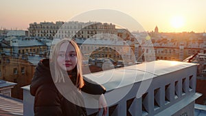 Portrait blonde smiling teen girl looks around on cityscapes from roof terrace.