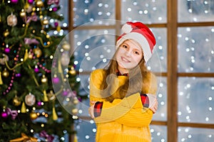 Portrait of blonde teen girl in red christmas hat on the background of Christmas tree