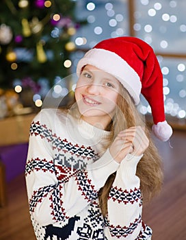 Portrait of blonde teen girl in red santa hat on the background of Christmas tree