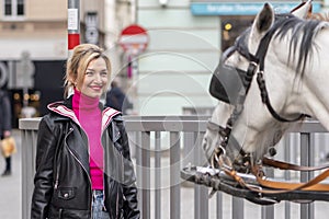 portrait of a blonde woman 35-40 years old, looking at a horse-drawn carriage in a European city.