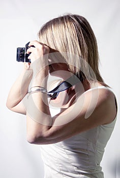 portrait of blonde woman with camera, intent on shooting, fair complexion dressed in light dress.