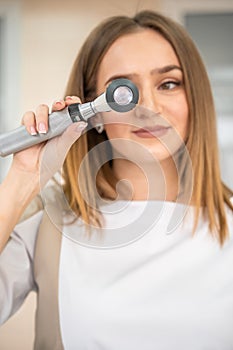 Portrait of blonde woman dermatologist with dermatoscope in uniform and gloves in doctor office before examination in