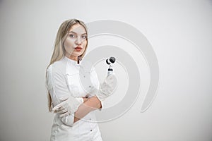 Portrait of blonde woman dermatologist with dermatoscope in white lab coat and white gloves on the white background