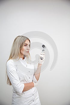 Portrait of blonde woman dermatologist with dermatoscope in white lab coat and white gloves on the white background.