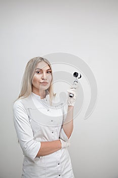Portrait of blonde woman dermatologist with dermatoscope in white lab coat and white gloves on the white background.