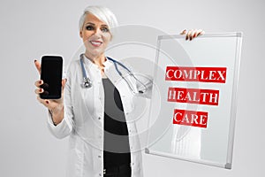 Portrait of blonde woman in doctors costume with a magnetic board and smartphone in her hands isolated on background