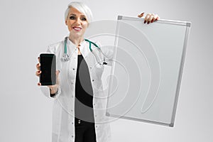 Portrait of blonde woman in doctors costume with a magnetic board and smartphone in her hands isolated on background