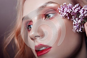 Portrait of a blonde woman with flower petals on her face close-up, bright red makeup and lipstick. Skin hydration, face care