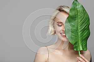 Portrait of blonde woman and green leaf. Organic cosmetics concept.