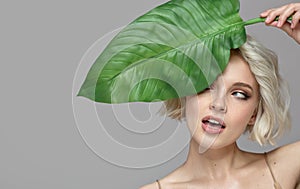 Portrait of blonde woman and green leaf. Organic cosmetics concept.