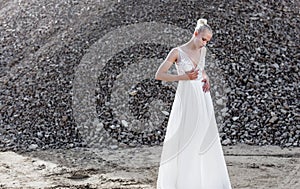 Portrait of blonde woman with hair tight up in white bride dress, in day time, over piles of stones