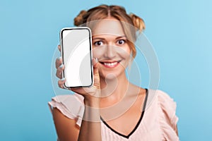Portrait of blonde woman standing with charming smile, happy expression and showing mobile device, cell phone with mock up empty