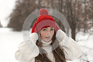 Portrait of blue-eyed girl in fashionable knitted red hat and mittens and woolen sweater in winter forest. Ladies knitwear