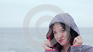 Portrait of a blue eyed woman in a jacket with a hood at the beach