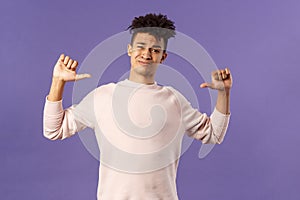 Portrait of boastful handsome young male student with dreads, bragging about how he workout in gym, show-off, pointing