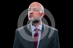 Portrait of a bold unshaven businessman in a grey suit ted tie and blue shirt on a black background