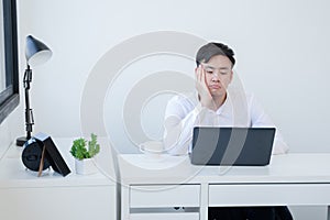 Portrait of bored Asian young handsome businessman wear white shirt working with laptop at office. Unmotivated employee
