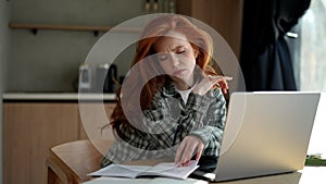 Portrait of bored female student studying using laptop sitting at desk in home. Exhausted woman cannot concentrate on