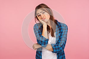 Portrait of bored lazy girl in checkered shirt leaning on hand and looking at camera with disinterest