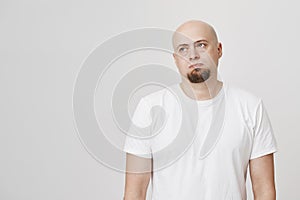 Portrait of bored and tired bald man with beard looking aside with gloomy expression, standing over gray background. Guy