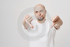 Portrait of bothered annoyed bald caucasian bearded man showing thumbs down, giving negative opinion while rolling eyes photo