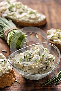 Portrait of a bowl of homemade cream cheese spread with chopped chives surrounded by bread slices with spread and a