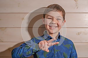 Portrait of a boy 8 years old brunette in a blue shirt. Shows two fingers.