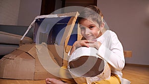 portrait of a boy with an astronaut helmet next to a cardboard toy spaceship
