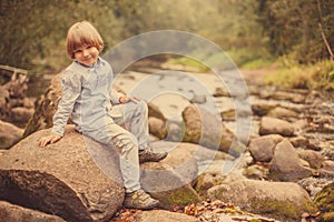 Portrait of a boy on a background of nature. The child is sitting on the rocks by the river