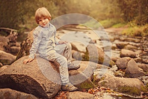 Portrait of a boy on a background of nature. The child is sitting on the rocks by the river