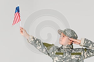 portrait of boy in camouflage clothing saluting and looking at american flagpole in hand