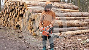 Portrait of boy with a chainsaw, stacked pine logs. Help child choose a career.