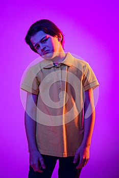Portrait of boy, child with unhappy, spoild facial expression isolated over purple background in neon light