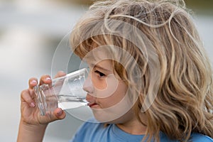 Portrait of boy drinking glass of water. Kid drinking water outdoor. Thirsty child.