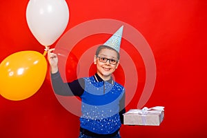 Portrait of a boy in a festive hat with colorful balloons and a box with a bow wrapped in silver paper.