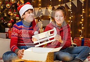 Portrait of a boy and girl in New Year decoration. They open a box, take out the sled and have fun. Holiday lights, gifts and a