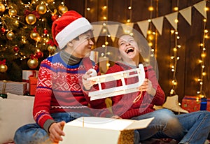 Portrait of a boy and girl in New Year decoration. They open a box, take out the sled and have fun. Holiday lights, gifts and a