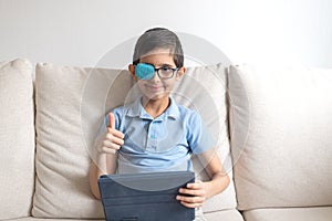 Portrait of boy in glasses with patch for glasses. Boy with tablet. Treat lazy eye, amblyopia, strabismus.  Remote learning. Dista