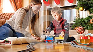 Portrait of boy with his mother playing on floor with toy train and railways. Child receiving presents and toys on New